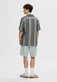 Camicetta a maniche corte con motivo geometrico bianco e nero, abbinata a pantaloni corti azzurri. La camicetta presenta una vestibilità rilassata e colletto piatto.