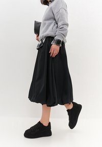 Czarna, obszerna spódnica w zestawieniu z szarym sweatshirtem i stylowymi czarnymi sneakersami ozdobionymi błyszczącymi akcentami.