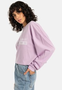 Lavender long-sleeve crop top with a soft cotton texture, featuring floral white prints across the chest and relaxed fit.