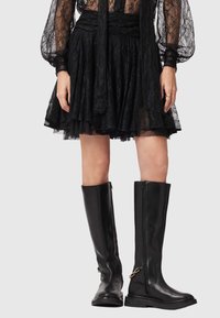 Bottes montantes en cuir noir avec fermeture éclair latérale, semelle plate et détails métalliques minimalistes. Texture lisse avec un design épuré.