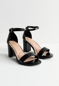 Czarne lakierowane sandały na wysokim obcasie z paskiem wokół kostki, szerokim przodem i blokowym obcasem oraz wyściełaną wkładką. Gładka tekstura, minimalistyczny design.