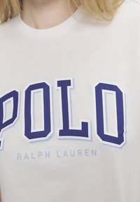 Vit bomull t-shirt med iögonfallande, marinblå "POLO"-tryck och ljusblå detaljer, med rund halsringning och korta ärmar.