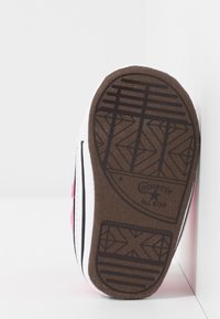 Rožinės drobės sportbačiai su guminiai padu, baltais siūlais ir akcentais, turintys tekstūruotą rudą padas su geometriniais raštais.