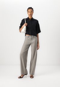 Camicia nera a maniche corte con bottoni, pantaloni ampi grigi chiari, sandali neri con tacco e una piccola borsa bianca. Texture lisce e vestibilità su misura.