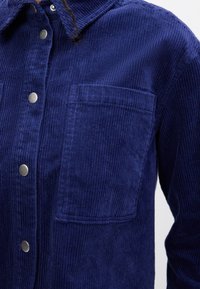 Giacca in corduroy blu navy con colletto, bottoni a pressione in argento e tasca sul petto con texture a righe verticali.