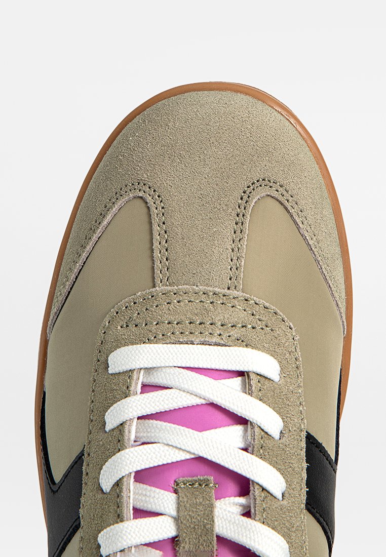Tan suède en textiel sneaker met witte veters, een roze tong en zwarte accenten, voorzien van een afgeronde neus en een gumrubberen zool.