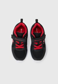 Des chaussures de sport noires avec un design en maille, des lacets rouges et une sangle Velcro. La semelle est blanche, avec un logo proéminent sur le côté.