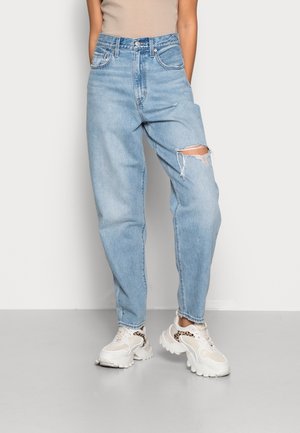  Lichtblauwe high-waisted jeans met een relaxte pasvorm en kniebesmettingen, gemaakt van denim met zichtbare stiksels. Gecombineerd met witte sneakers.
