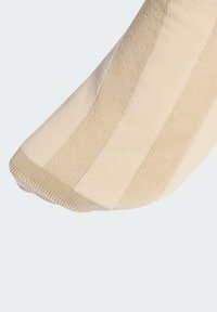 Beżowa skarpetka w pionowe paski, wykonana z miękkiego, teksturowanego materiału. Posiada wzmocnione noski i gładką, górną krawędź.