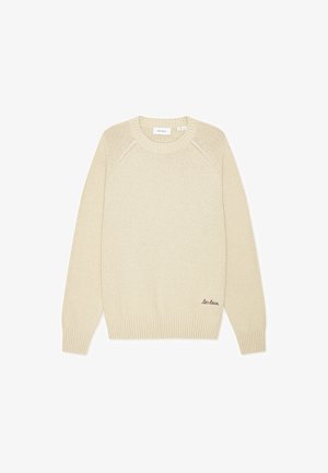 Beige strikkegenser med rund hals, ribbestrikkede mansjetter og kant, med en subtil logo-brodering nederst til venstre.