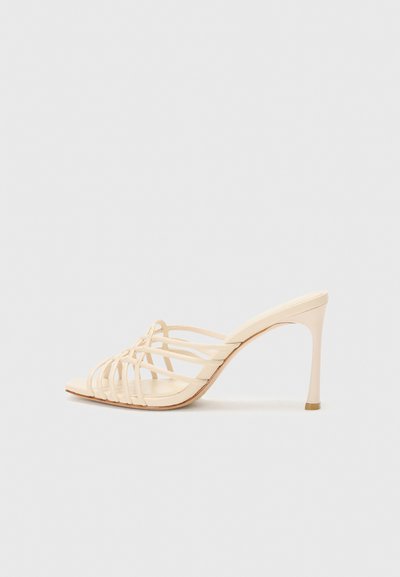 Beige high-heeled mules with a strappy design. Features a square toe, a smooth texture, and a slender heel with a gold accent at the base.