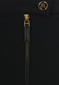 Gonna nera in tessuto con zip e hardware dorati, caratterizzata da un design elegante e una texture liscia. Nota accentuata con bottone logo in vita.