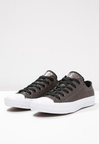 Baskets en mesh noir avec semelles en caoutchouc blanches, bouts ronds et lacets noirs. Présentent des détails cousus sur la tige et une surface texturée.