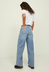 Jeans in denim azzurro chiaro, a gamba larga e vita alta, con due tasche posteriori e orlo sfilacciato. Abbinati a una t-shirt bianca e scarpe nere.