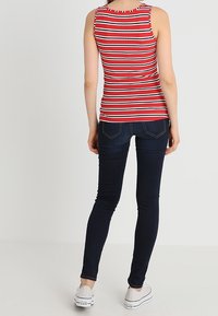 Top sin mangas a rayas rojas y blancas, con textura acanalada, combinado con jeans ajustados azules oscuros y zapatillas blancas, visto desde la parte posterior.