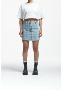 Person wearing a white crop top, light blue denim skirt with belt, and black lace-up combat boots standing on white background.