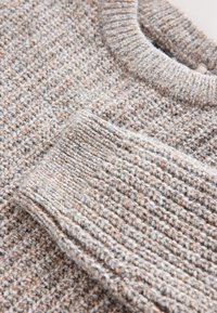 Lysegrå strikket sweater med et tekstureret mønster og en ribbet rund halsudskæring, med bløde fibre og antydninger af beige over det hele.