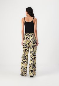 Black tank top and vibrant wide-leg trousers with a green and brown leaf pattern, featuring a drawstring waist and loose fit.