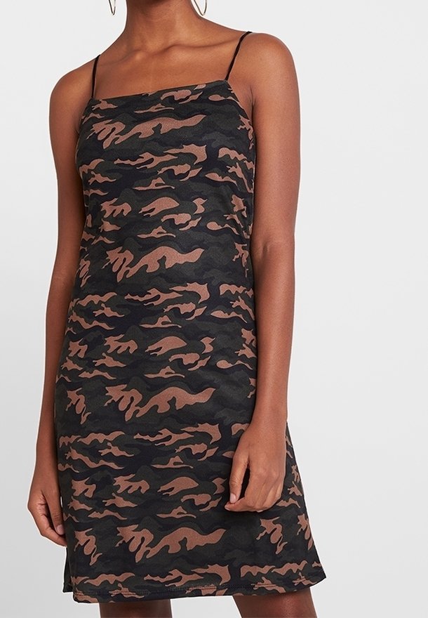 Femme portant une robe sans manches à motif camouflage noir et marron avec de fines bretelles spaghetti.