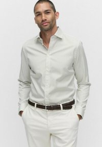 Witte button-up shirt met dunne groene verticale strepen, lange mouwen en een kraag, gecombineerd met lichte broeken en een bruine gevlochten riem.