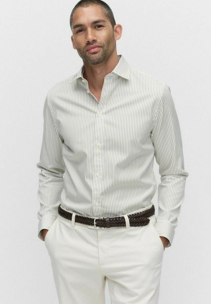 Witte button-up shirt met dunne groene verticale strepen, lange mouwen en een kraag, gecombineerd met lichte broeken en een bruine gevlochten riem.