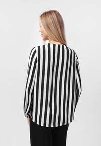 Svart og hvit stripet bluse med lange ermer og rund hals. Myk, glatt stoff; buet hem bak.