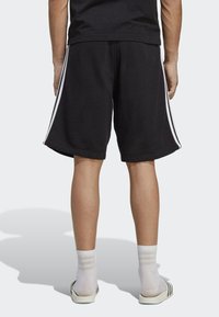 Juodi sportiniai šortai, pagaminti iš medvilnės. Su baltais šonų juostelėmis. Aviami su baltais kulkšninių kojinių ir šlepečių. Atsitiktinis dizainas ir prigludimas.