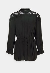 Blouse noire à manches longues boutonnée, avec un détail en dentelle sur le yoke, des poignets froncés et une ceinture nouée à la taille.