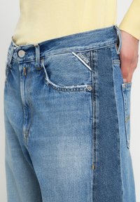Τζιν παντελόνι από denim με ανοιχτό μπλε πλύσιμο και μοναδικό σχέδιο χρωματικών μπλοκ. Διαθέτει ξεφτισμένο στρίφωμα, τσέπες κανονικού μεγέθους και διακριτικές ραφές.