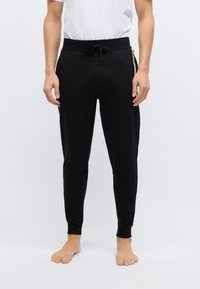 Czarne spodnie dresowe typu jogger z regulowanym pasem na sznurek, zwężanym krojem i ściągaczami przy nogawkach. Gładka tkanina z kontrastującymi paskami po bokach dla podkreślenia detali.