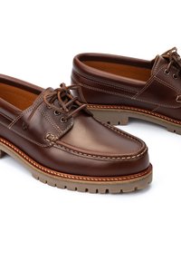 Chaussures en cuir marron avec une finition lisse, présentant un design de style mocassin, un système de fermeture à lacets et une semelle en caoutchouc robuste. Coutures blanches en accent.