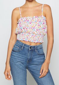 Blommig croptop med volangdekorerad halsringning och justerbara axelband; har en resår i midjan. Matchas med högmidjade blå jeans.