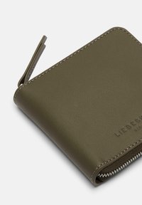 Portfel z oliwkowej skóry o fakturowanej powierzchni, z wytłoczonym logo i kontrastującymi przeszyciami. Posiada zamknięcie na zamek błyskawiczny oraz zaokrąglone krawędzie.