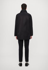 Black trench coat with a high collar, long sleeves, and a straight cut, paired with dark trousers and shoes. Simple design, smooth texture.