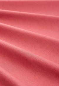 Katoenen stof in een zachte koraalkleur met een gladde, licht gestructureerde oppervlakte, met zachte plooien en draperingen.