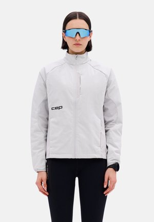 Person wearing a white zip-up jacket with "cep" logo, black leggings, blue reflective sports sunglasses, and a black wristwatch, standing front-facing.