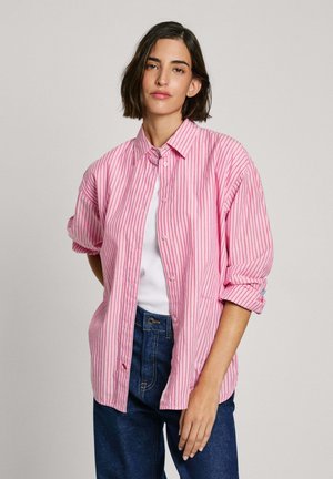Roze en witte gestreepte button-up shirt, losse pasvorm, met opgerolde mouwen. Draagt over een witte top, gecombineerd met donkere spijkerbroek.