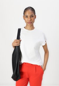 Vit bomulls t-shirt med rund halsringning, matchad med röda skräddarsydda byxor. Modellen håller en stor svart läderaxelväska.