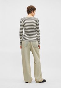 Μαύρη και κρεμ ριγέ μπλούζα μακρυά μανίκια με στρογγυλή λαιμόκοψη, συνδυασμένη με ανοιχτό μπεζ παντελόνι φαρδιάς γραμμής. Μινιμαλιστικός σχεδιασμός.