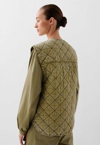 Oliegroen gewatteerd vest met diamantpatroon, zachte textuur en ronde zoom, gelaagd over een bijpassend longsleeve shirt. Achteraanzicht weergegeven.