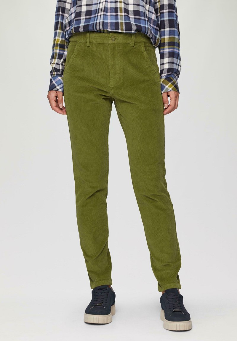 Groene corduroy broek met een slanke pasvorm, met een knoopsluiting en voorzakken, gecombineerd met donkere sneakers. Geruite shirt zichtbaar op de achtergrond.