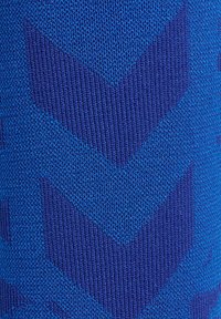 Blått mönstrat tyg med en zick-zack-design. Materialet verkar vara stickat, med olika nyanser av blått som skapar textur och djup.