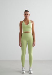 Lysegrønn sports-bh og tights-sett, sømløs design, utskjæring detalj i midjen, parret med hvite treningssko.