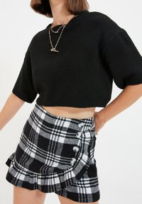 Maglione nero corto con maniche corte, abbinato a una mini gonna a quadri bianca e nera con bottoni argentati e orlo arricciato.