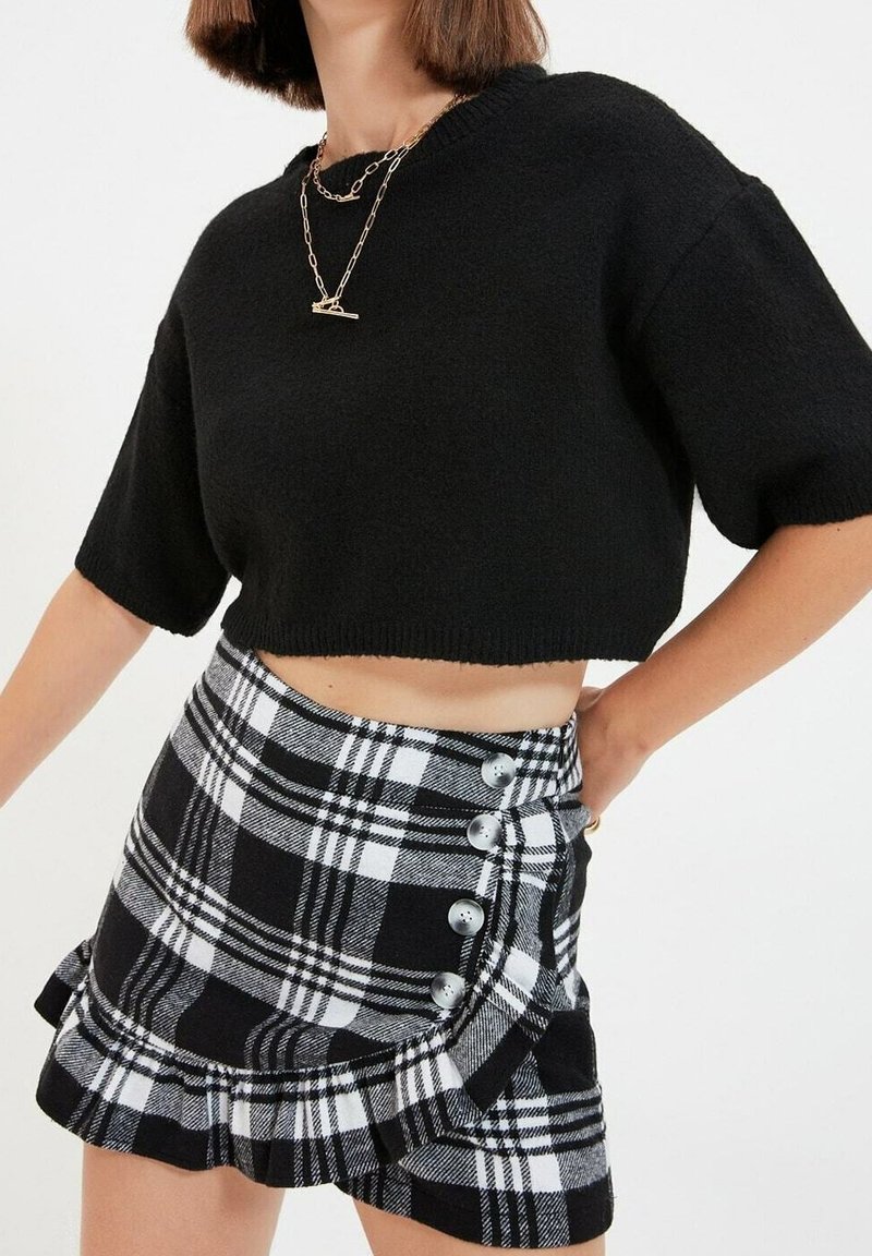 Maglione nero corto con maniche corte, abbinato a una mini gonna a quadri bianca e nera con bottoni argentati e orlo arricciato.
