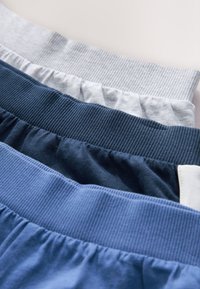 Patru perechi de benzi elastice cu dungi pe talie la pantaloni casual pliați, în nuanțe de albastru și gri.