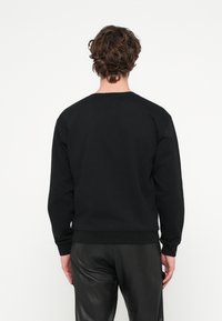 Čierna mikina s dlhými rukávmi, rebrovanými manžetami a lemom, mäkký materiál, zaoblený výstrih, jednoduchý dizajn, nosená s čiernymi koženými nohavicami.