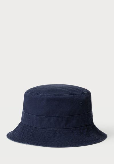 Chapeau seau en coton bleu marine avec un dôme structuré, deux bandes horizontales et un large bord plat. Comprend de la texture et des oeillets de ventilation.