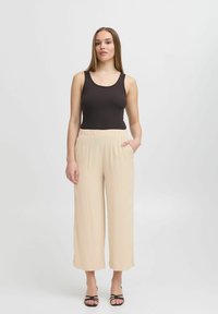 Zwarte geribbelde tanktop gecombineerd met beige wijde broek met een elastische tailleband en zijzakken. Zwarte sandaaltjes met bandjes maken de outfit compleet.