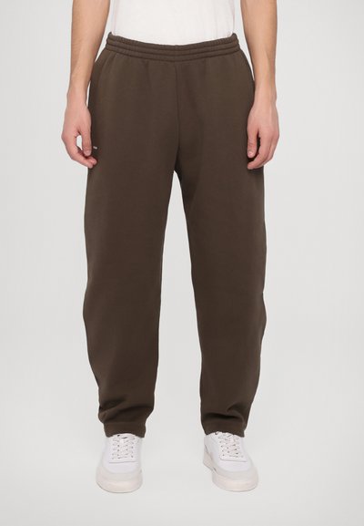 Καφέ φόρμες με ελαστική μέση, χαλαρή εφαρμογή και πλαϊνές τσέπες. Συνδυασμένες με λευκά αθλητικά παπούτσια για αντίθεση.